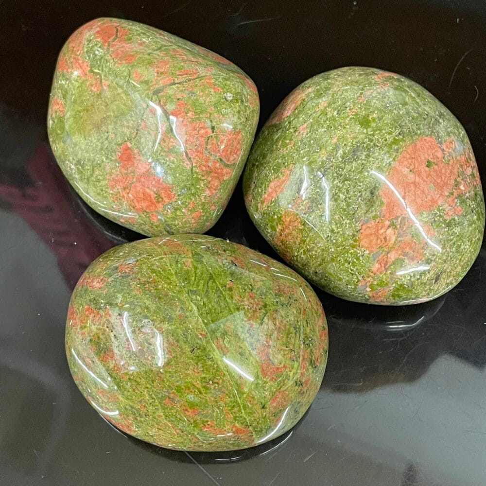 Three Unakite Granite stones, with their striking mix of green and pink hues, rest elegantly on a dark surface.