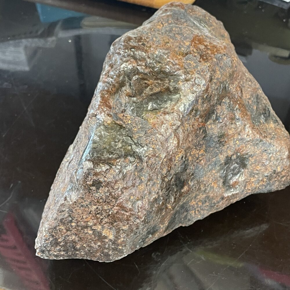 The Campo del Cielo Iron Meteorite from a high-end estate collection weighs 15.1 lbs (6850g) and displays a rough, dark brown and gray triangular form atop a reflective black surface.