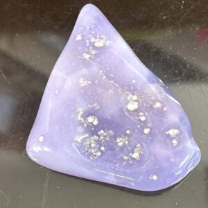 A smooth, glossy Rare Holly Blue Calapooia Agate 31g or 155cts with white specks rests on a reflective black surface.