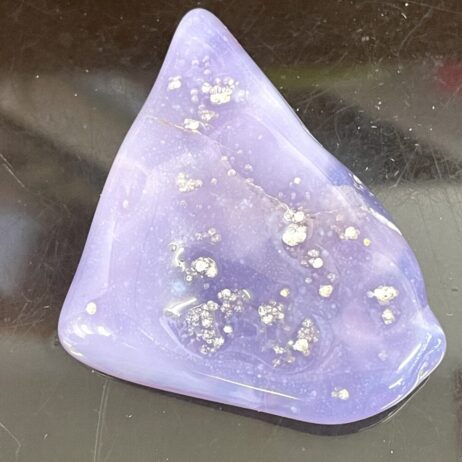A smooth, glossy Rare Holly Blue Calapooia Agate 31g or 155cts with white specks rests on a reflective black surface.