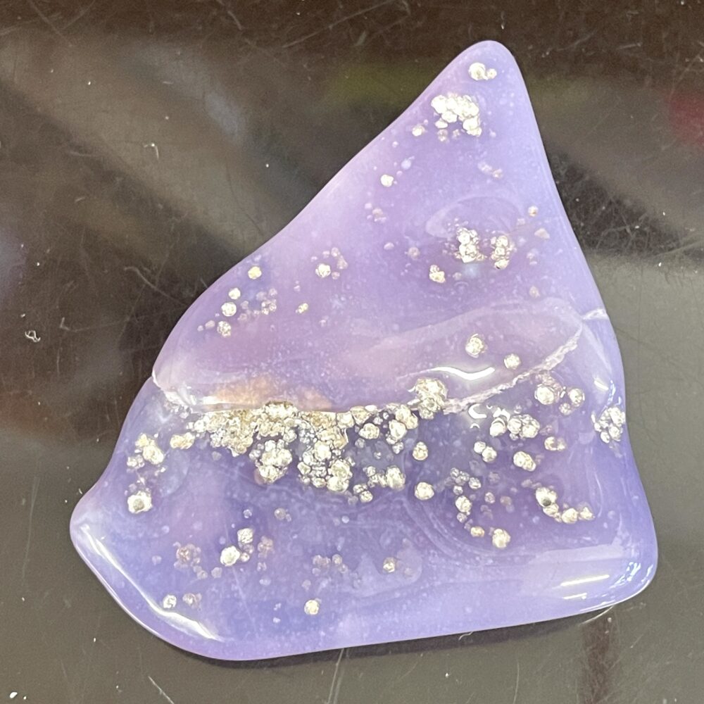 A smooth, triangular crystal with reflective speckles sits on a dark surface, reminiscent of Rare Holly Blue Agate 31g or 155cts.
