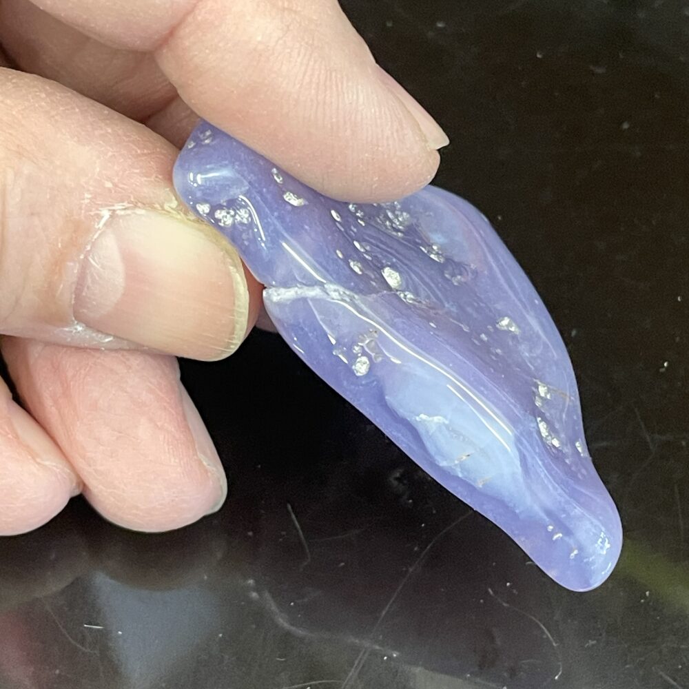 A hand gently cradles a smooth, translucent Rare Holly Blue Agate 31g or 155cts, its surface flecked with scattered white specks against a dark backdrop.