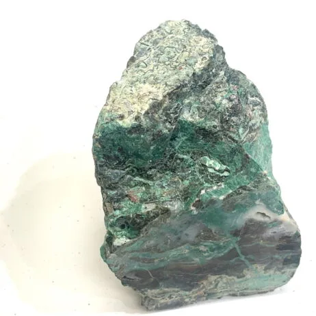 A rough, unpolished Malachite with apparent agate-like quartz veins and a hint of azurite rests on a white surface, displaying mottled dark and light green coloration.