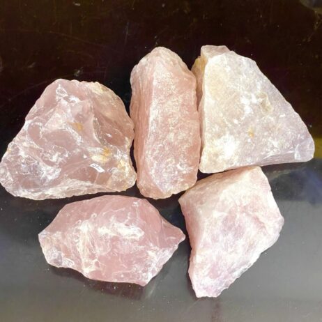 Five Rose Quartz Rough stones, each up to 3 inches, are displayed on a dark surface. Their pink shapes and sizes vary.
