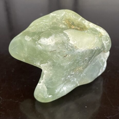 The Prehinite natural shaped tumble polished 68.4 grams features a translucent green hue and irregular form on a dark, reflective surface.