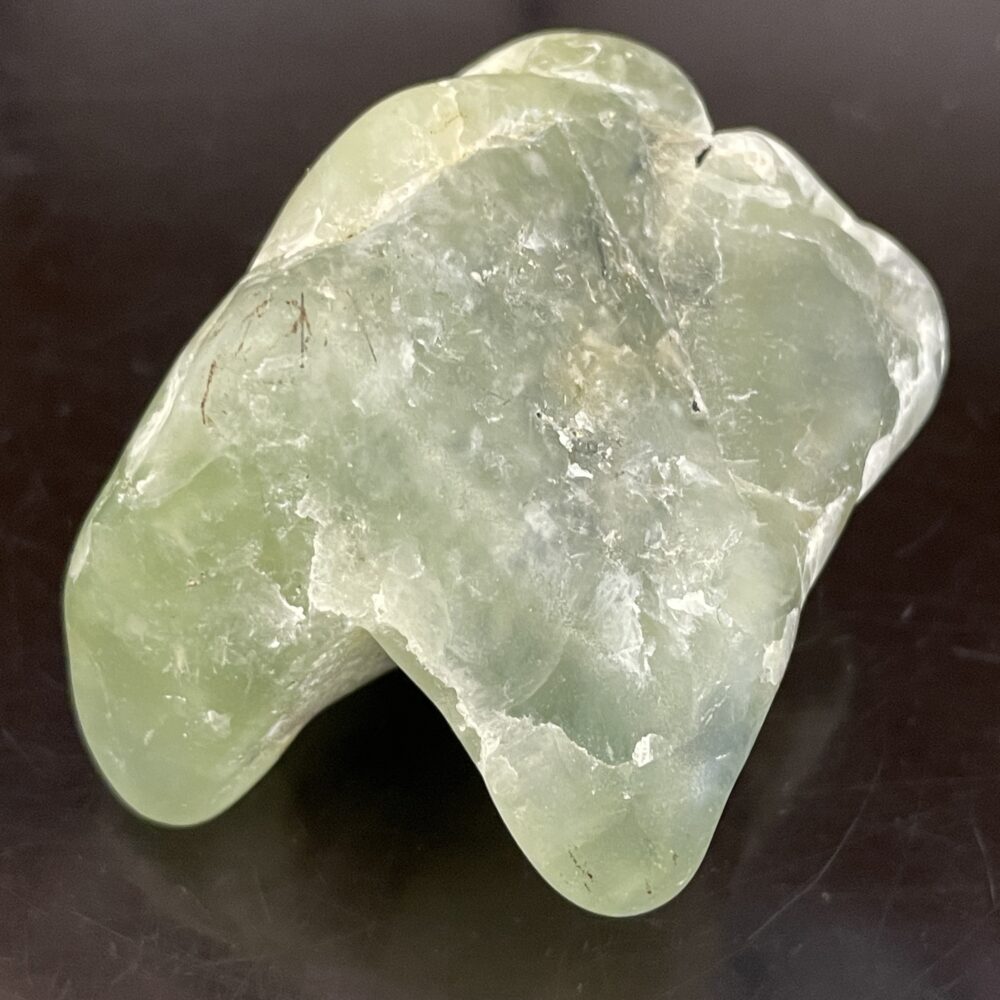 A smooth, translucent light green Prehinite tumbled stone (68.4g/2.4oz) with uneven surfaces on a dark, reflective background.