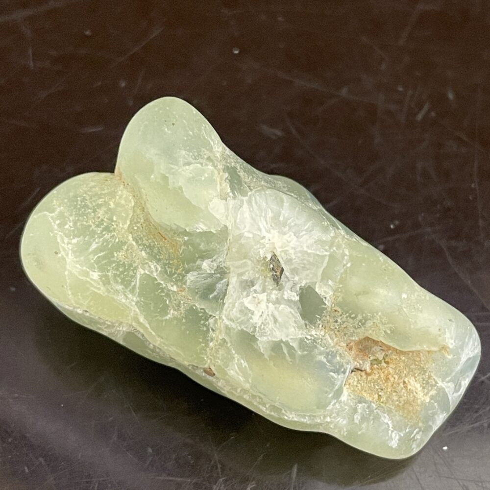 A translucent, pale green Prehinite tumble polished specimen, 68.4 grams (2.4 oz), with rough surfaces on a dark background.
