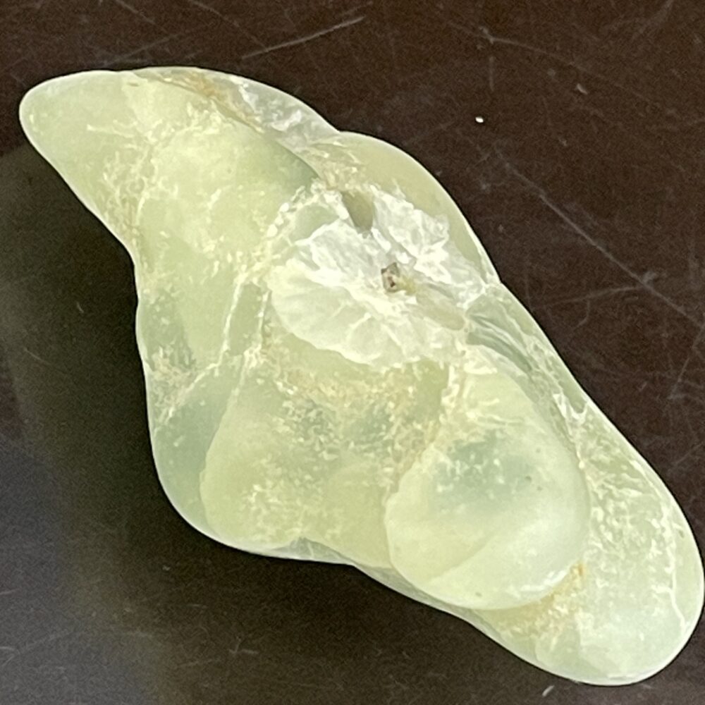 The Prehinite Natural Shaped Tumble Polished 68.4 grams has a smooth, slightly translucent pale green surface on a dark background.