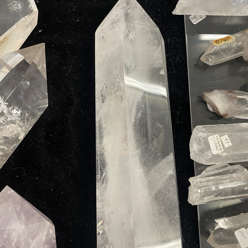 The Rare Self Healed Lemurian Quartz Crystal Showing Hematite, measuring 5.5 inches long, is displayed upright on a black surface, surrounded by several smaller quartz crystals.