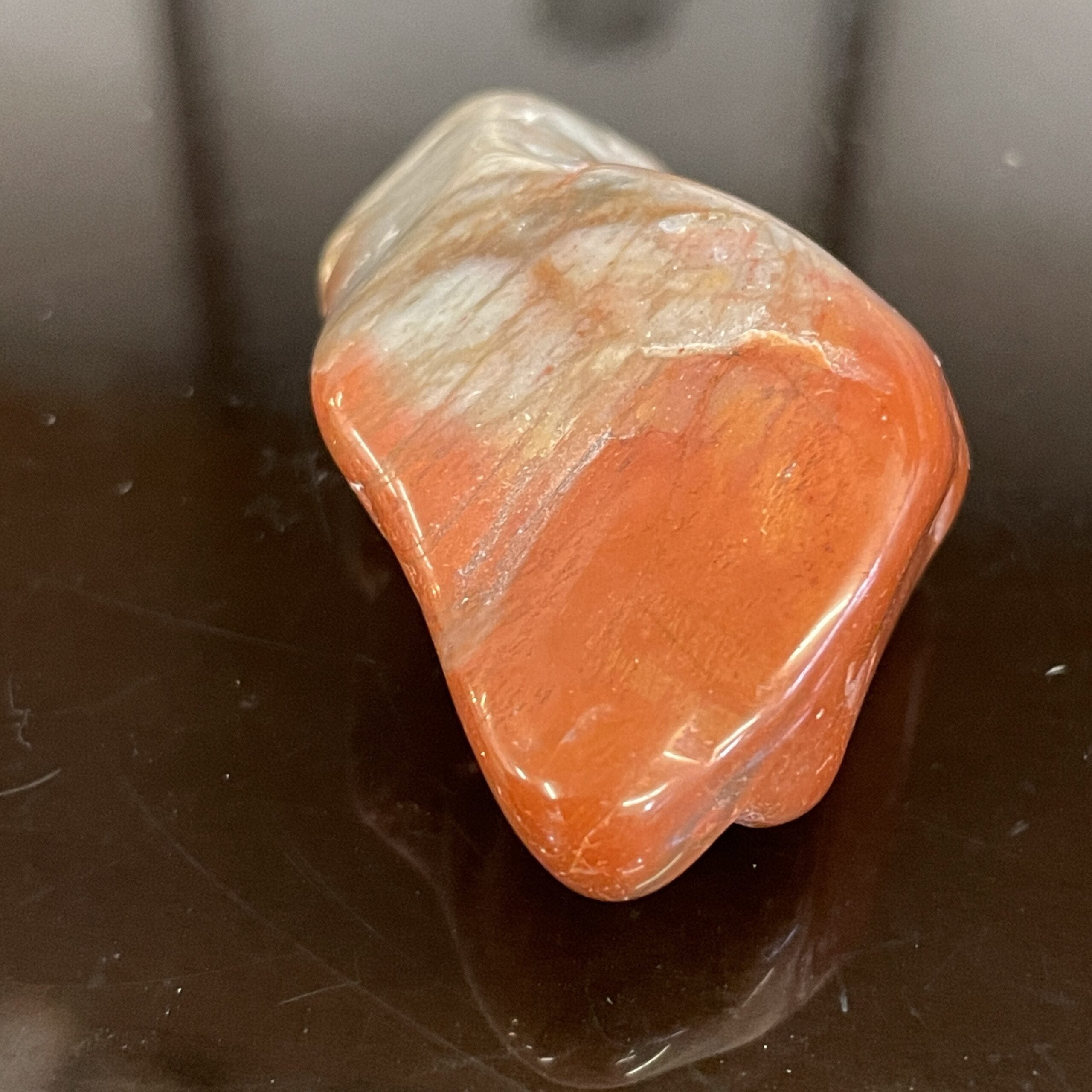 An Arizona Rainbow Petrified Wood Polished Chunk Specimen, featuring red and white hues, rests on a shiny black surface.