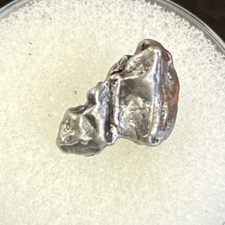 The IM26 Campo del Cielo Iron Meteorite Nice 1.55g Specimen, small and uniquely shaped, is displayed on a textured white surface.