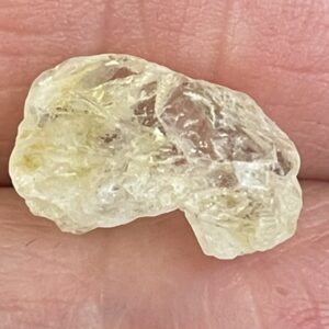 A close-up of the Phenakite - Phenacite Crystal from Brazil 3.50 ct, showcasing its rough, translucent yellowish form resting on a finger.