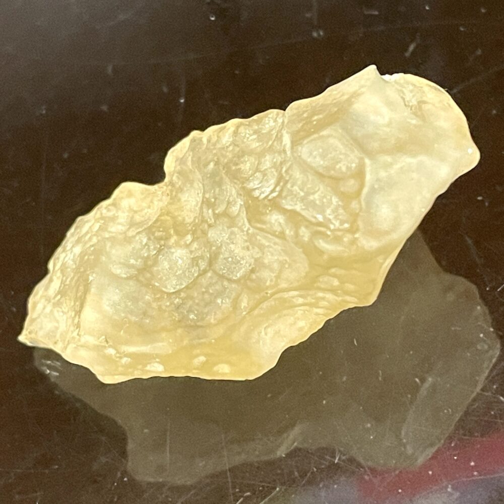 A close-up image of a translucent, yellowish, irregularly shaped object with a rough texture, placed on a reflective dark surface.