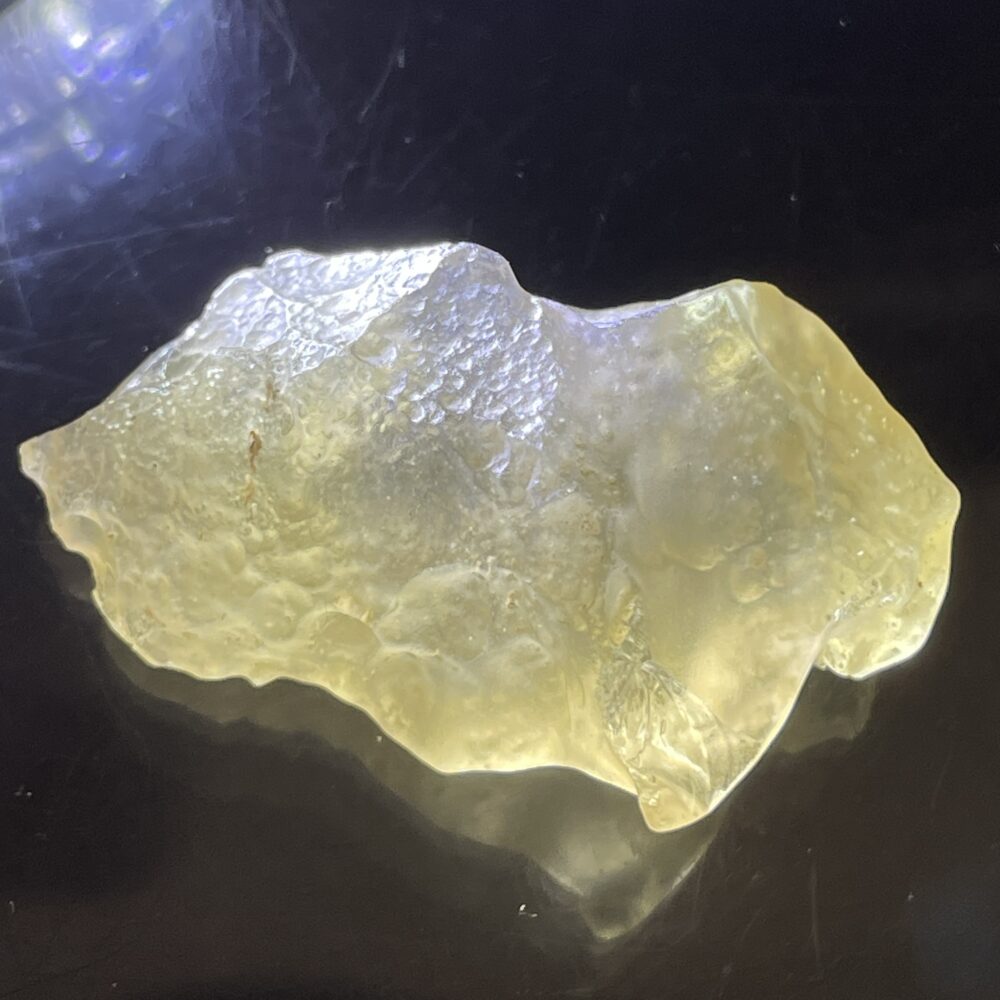 A translucent yellowish mineral or resin fragment with a rough, irregular surface, displayed on a black background.