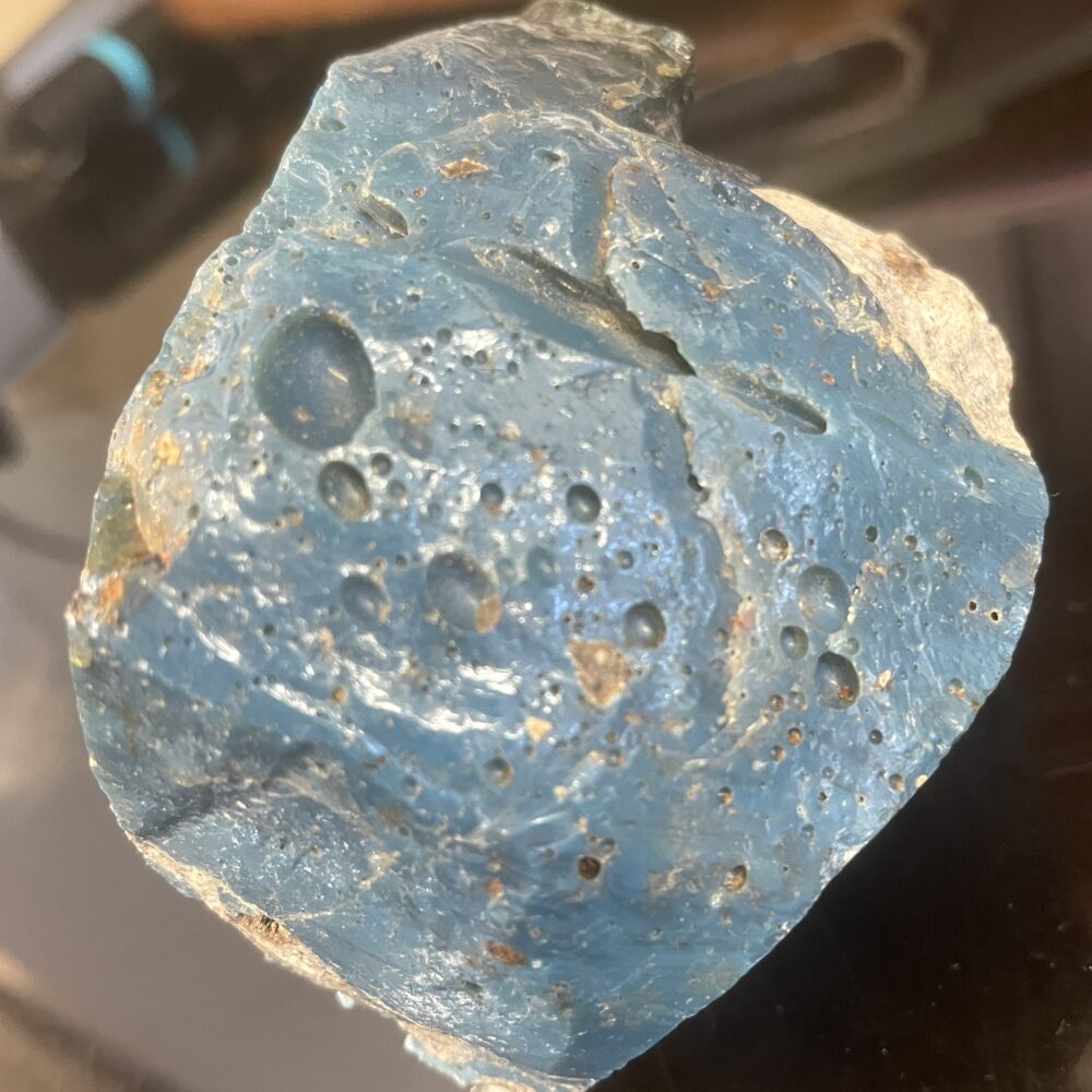 A close-up of a blue, porous rock with various holes and indentations on its surface, resting on a dark background.