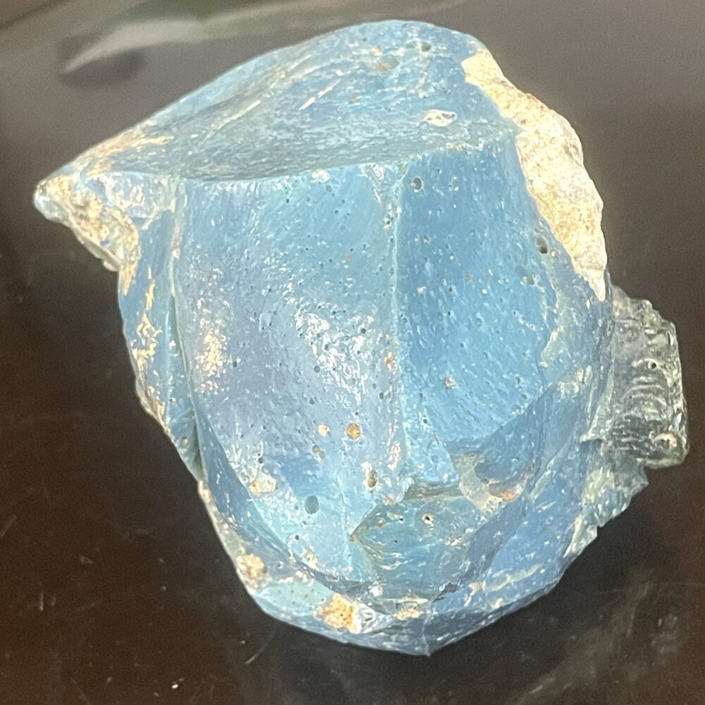 A rough, blue, irregularly shaped rock with some lighter patches and small surface holes, resting on a black background.