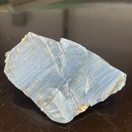 Leland Blue Slag Glass Showing Several Shades of Blue - 2.6 oz (73 g), features rough, translucent surfaces and striations in captivating blue tones, displayed on a dark reflective surface.
