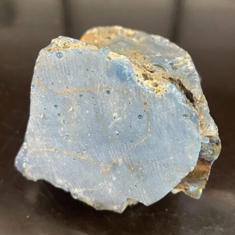 A Leland Blue Slag Glass, 6.4 oz/171g, showing several shades of blue with visible natural cracks and surface imperfections, displayed against a dark background.