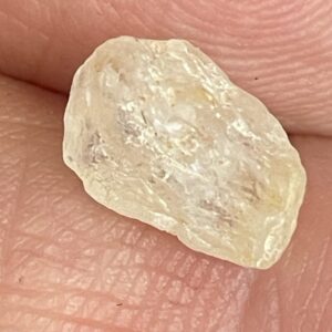 A close-up of Product, a rough, translucent off-white stone, resting on the ridged surface of a persons fingers.
