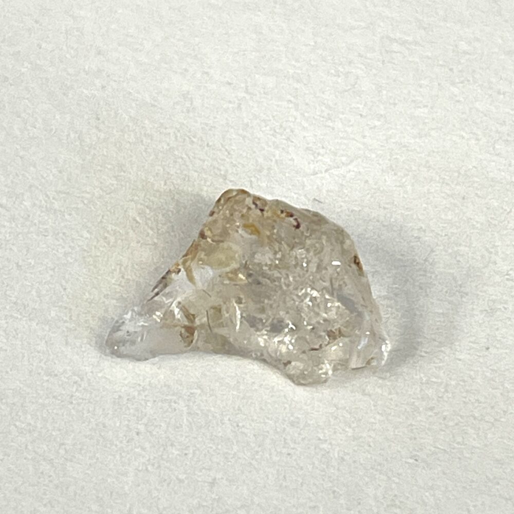 A rough, translucent crystal with slight brownish and clear areas sits on a plain white surface.