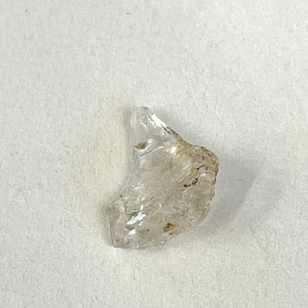A small, irregularly shaped translucent crystal with rough edges resting on a plain white surface.