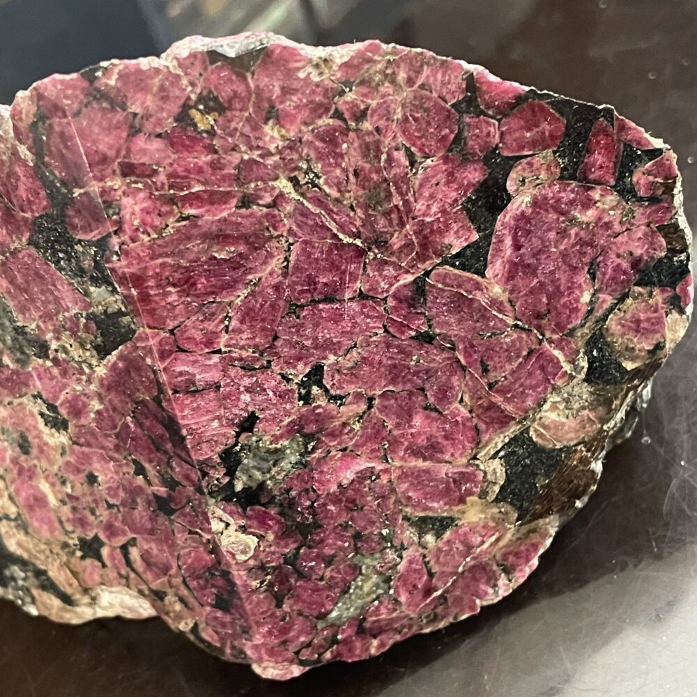 A large, rough mineral specimen featuring dense clusters of deep reddish-pink crystals with black and beige matrix on a dark surface.