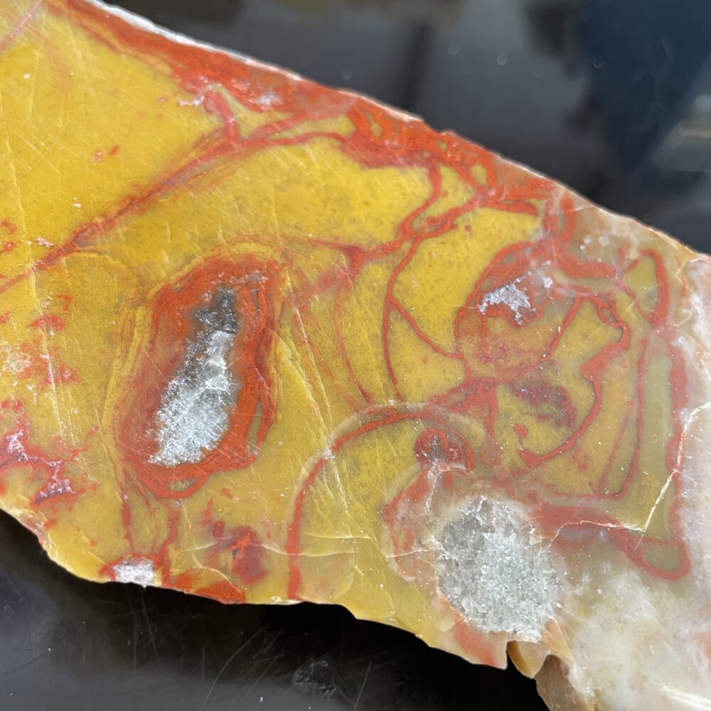 A close-up of a polished yellow and red jasper stone with visible quartz crystal inclusions on a dark surface.