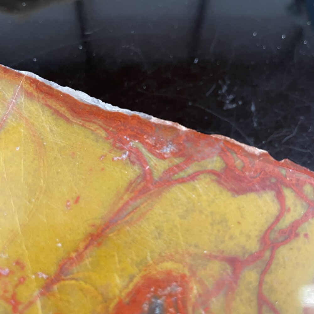 Close-up of a polished stone with yellow and red marbled patterns against a black background.