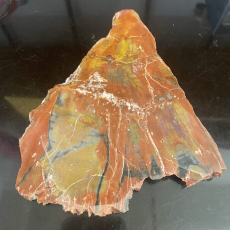 The Arizona Rainbow Petrified Wood - Beautiful Polished Specimen 201 g (7.1 oz) – features vibrant red, orange, yellow, and dark gray streaks, displayed as a polished piece on a black surface.