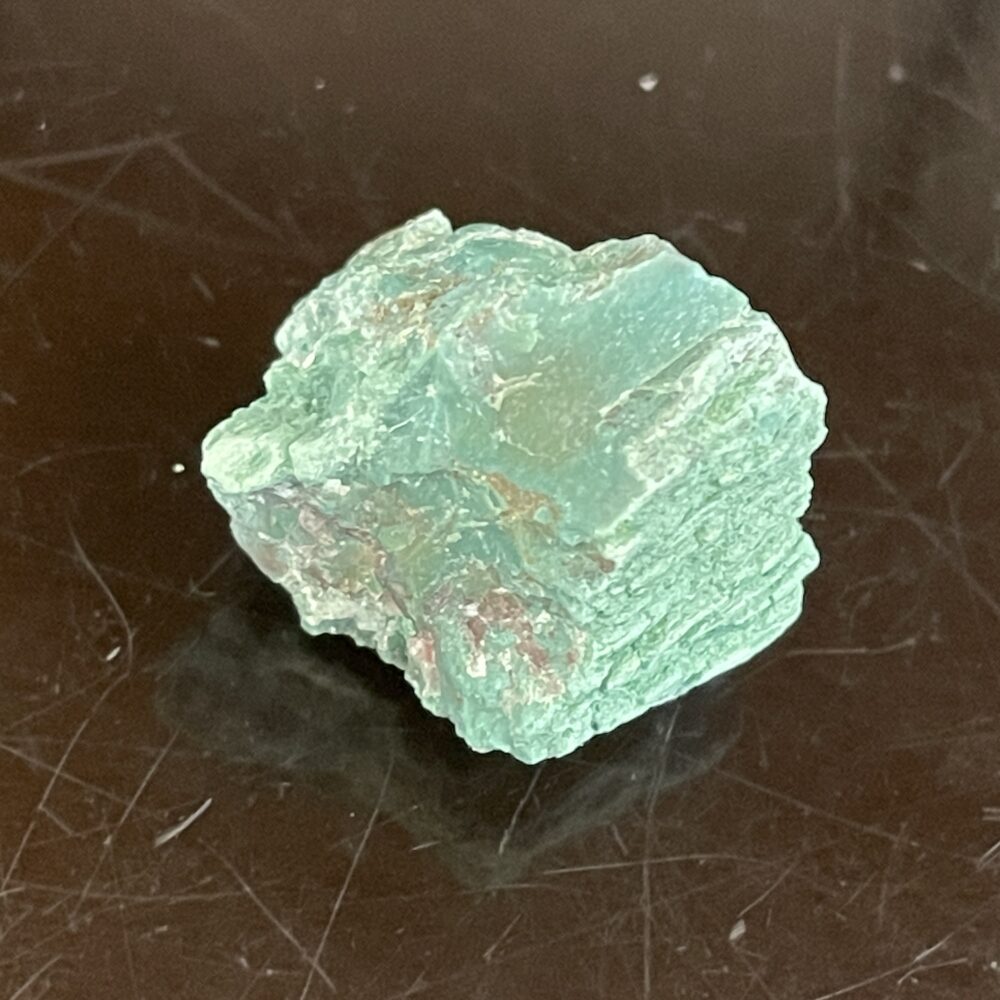 A rough Rare Green Chromium Petrified Wood specimen with a jagged texture, displayed on a reflective dark surface.