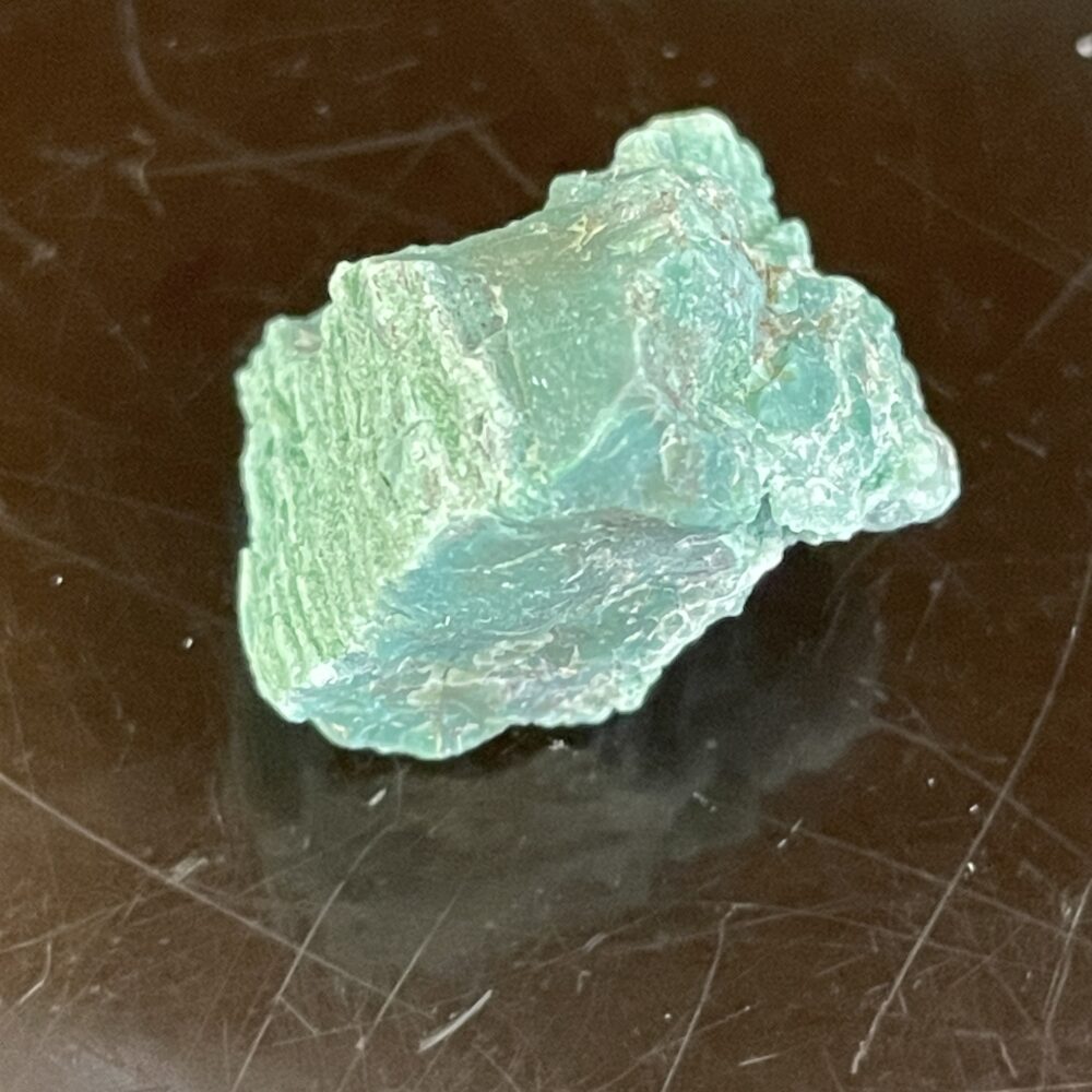 A rare Green Chromium Petrified Wood crystal, 6.16g (30.85 cts), featuring a rough, light green surface, rests on a dark, reflective background.