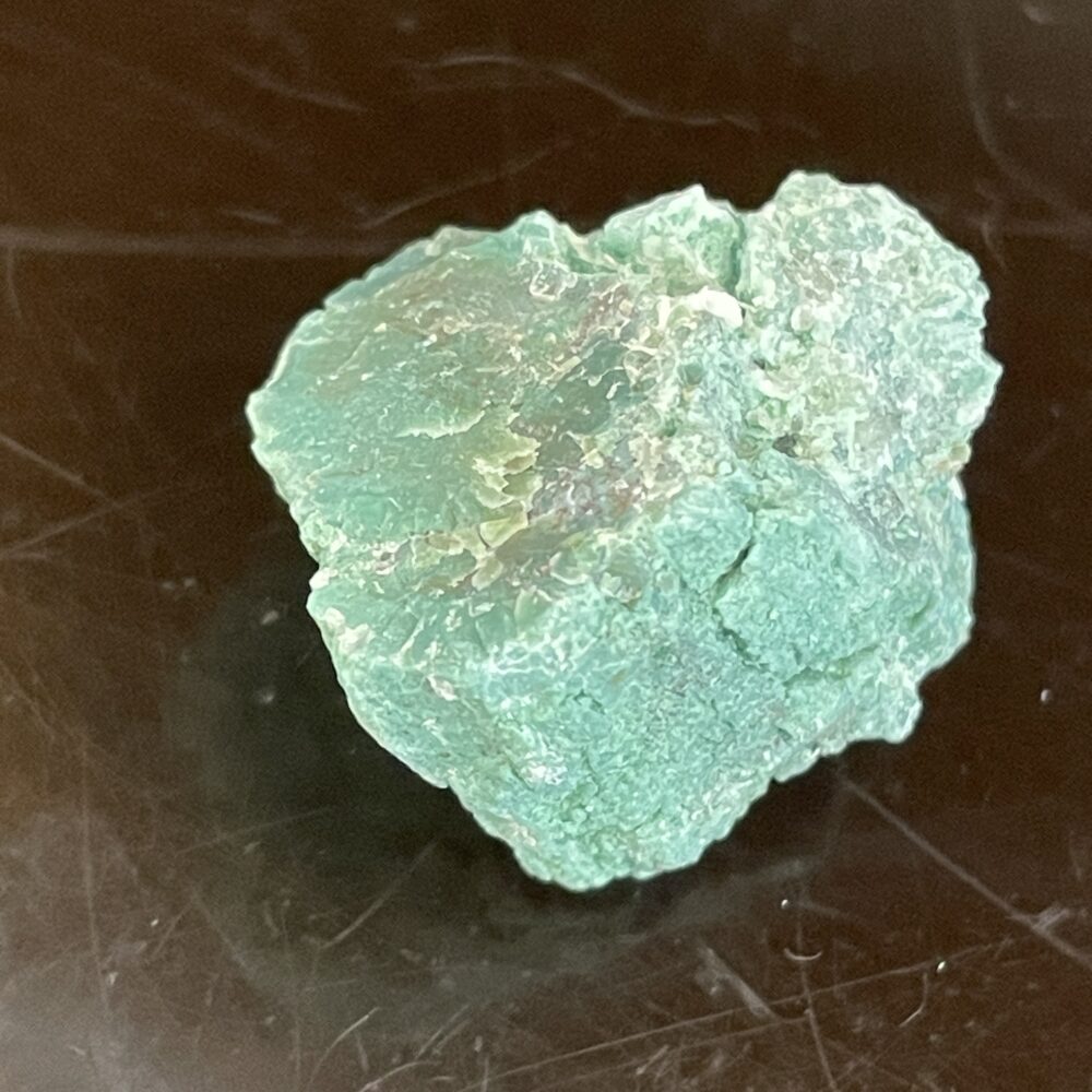 A Rare Green Chromium Petrified Wood specimen with a textured, unpolished surface rests on a dark, reflective background.