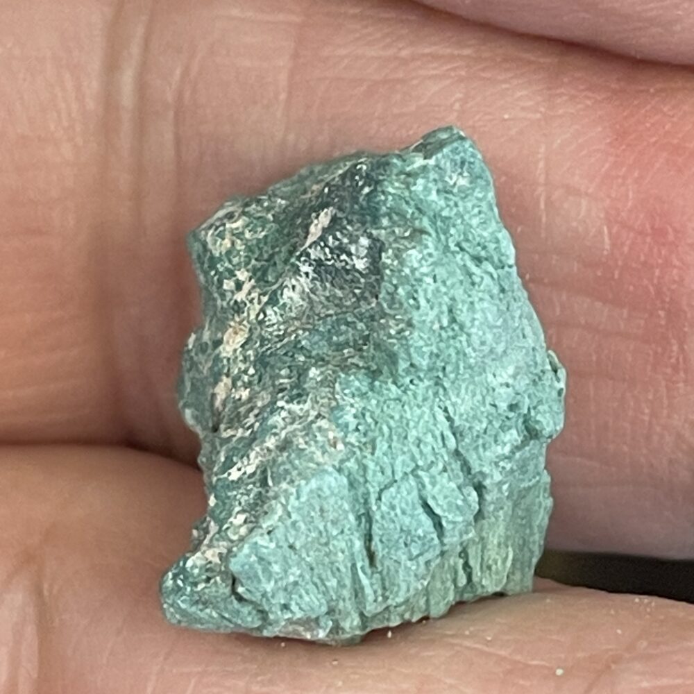A close-up of the Rare Green Chromium Petrified Wood 4.5g (22.70 cts), a rough turquoise-green specimen, held between two fingers.