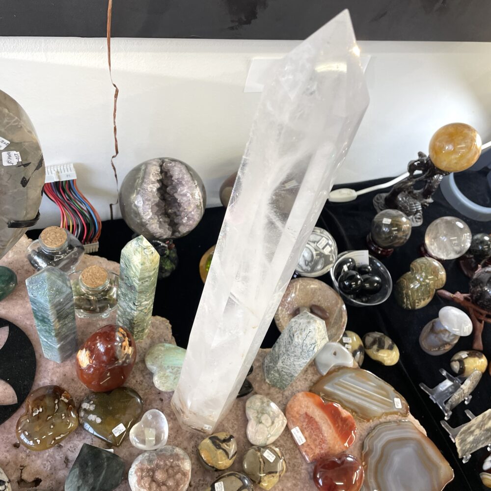 The rare 19.8-inch monumental quartz crystal, weighing 6 lbs 12 oz, stands upright among polished stones and mineral specimens.