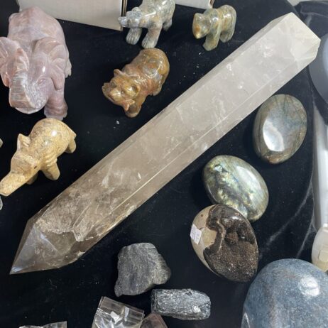 Showcasing the Rare 19.8 Inches Long Milky and Clear Quartz Crystal (6 lbs 12 oz) surrounded by polished gemstone animal figurines and assorted smooth and rough stones on a black surface.