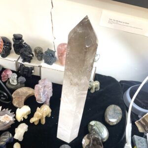 A tall, smoky quartz crystal tower stands upright among small carved animal figurines and polished stones on a tabletop display.