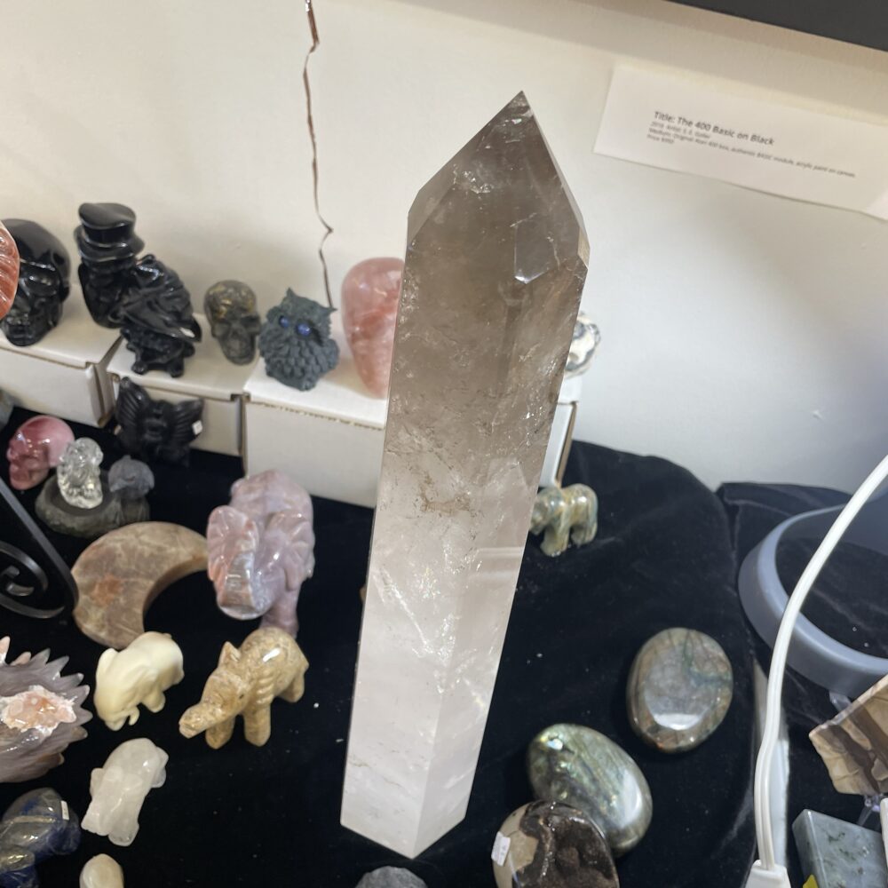 A Rare 19.8-inch Milky and Clear Quartz Crystal (6 lbs 12 oz, 3068g) stands upright on a black surface, its brilliant clarity catching the light among carved stone animal figurines and polished stones.