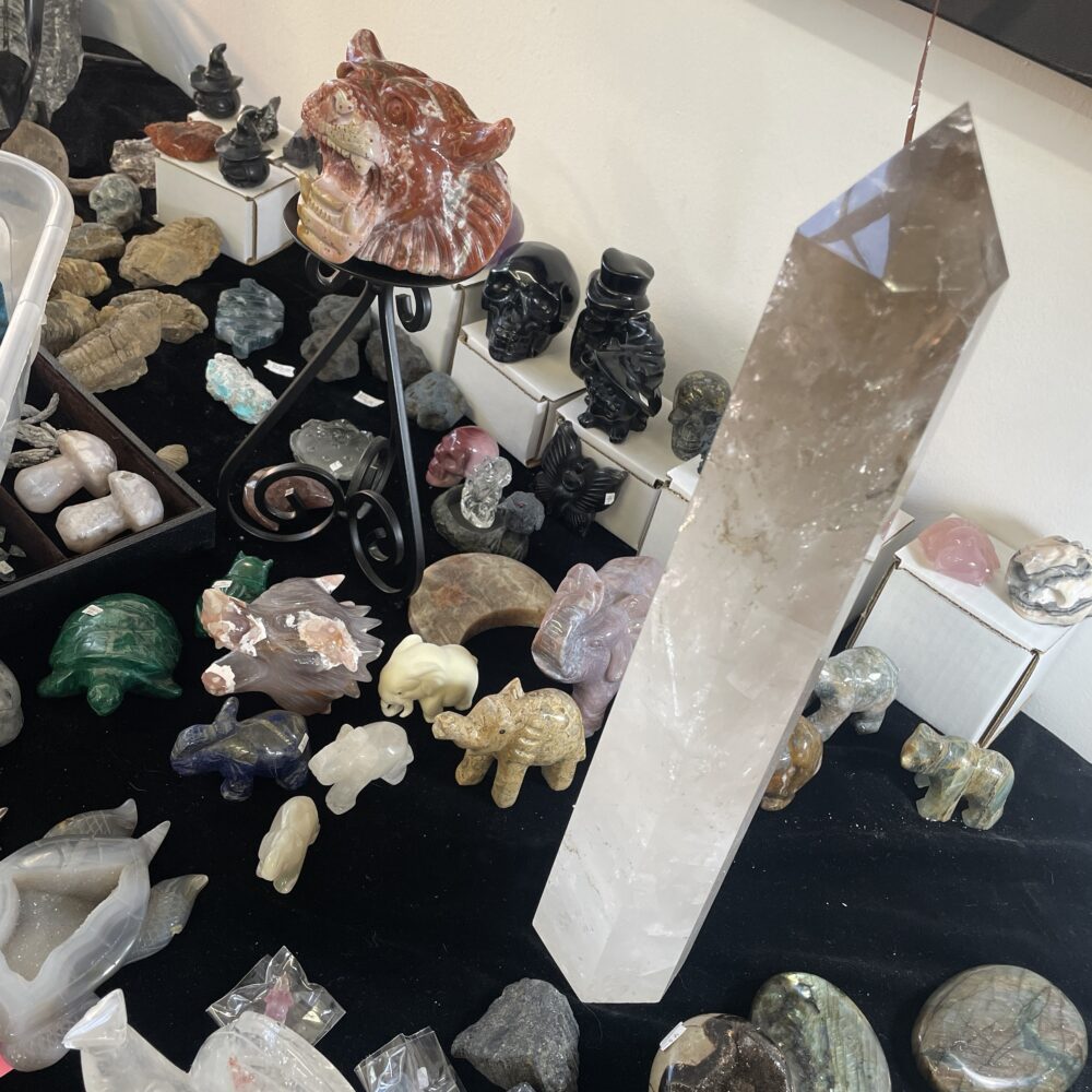 A Rare 19.8-inch Long Milky and Clear Quartz Crystal (6 lbs 12 oz) is displayed on a black cloth-covered table alongside carved stone animals and crystal figurines.
