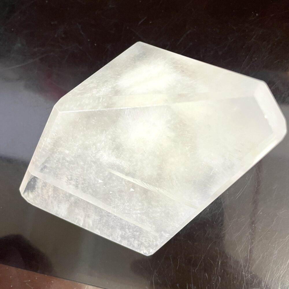 A rare Okenite inside Optical Calcite (Icelandic Spar) from India, weighing 14.7 oz (418g), with hexagonal clarity and flat faces, displayed on a dark, reflective surface.