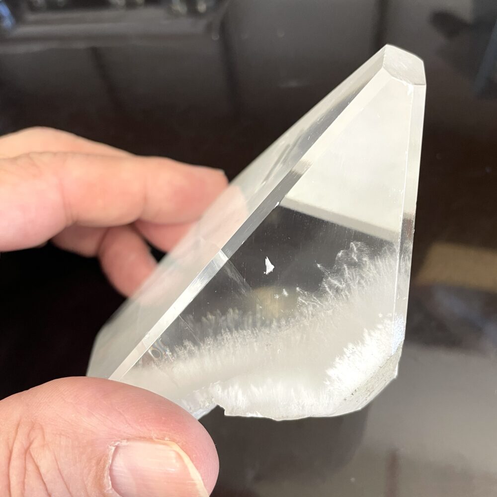 A hand displays rare Okenite in Optical Calcite from India, with frosted white patterns and a chipped edge against a dark background.