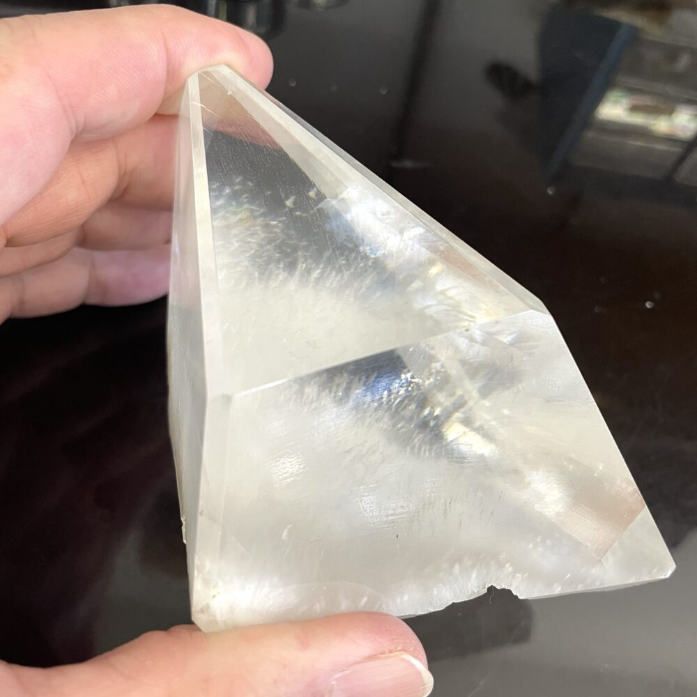 A hand holds a rare Okenite inside Optical Calcite from India, 14.7 oz—clear, pyramid-shaped, smooth surface, dark background.