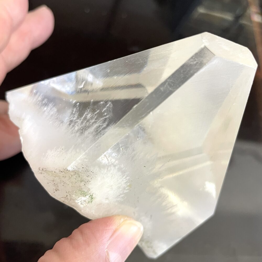 A hand holds Rare Okenite inside Optical Calcite from India, 1 lb 4.9 oz, with clear facets, white inclusions, and green specks.
