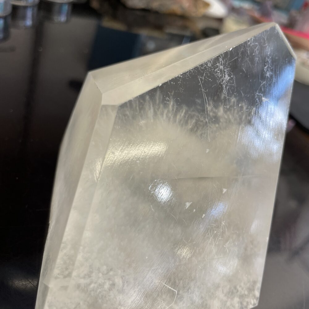 A polished crystal of Optical Calcite (Icelandic Spar) with rare Okenite inclusions from India sits on a dark surface, showing striations.