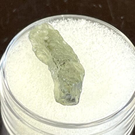 A .34 g (1.70 ct) Moldavite from Chlum, CZ is displayed on a white foam pad inside a clear round container.