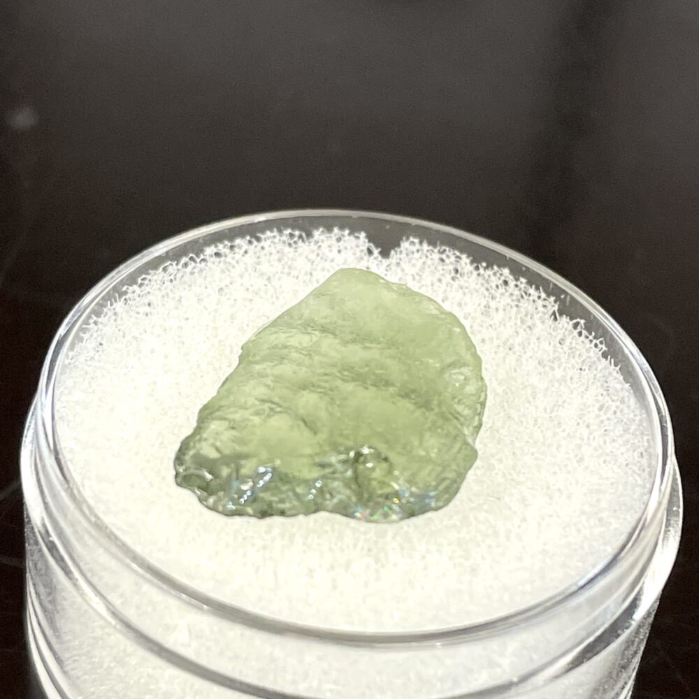 A 1.02 g (5.10 ct) green, translucent Moldavite from Chlum, CZ, displayed on white foam in a clear plastic container.