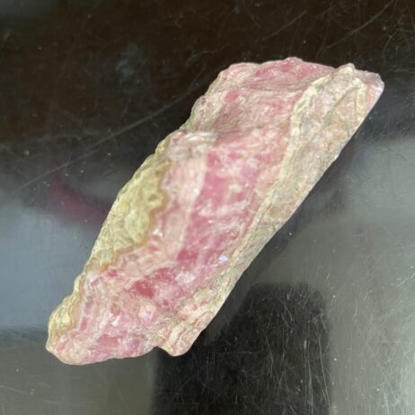 A beautiful old stock Rhodochrosite specimen with pink and tan hues rests on a reflective dark surface.