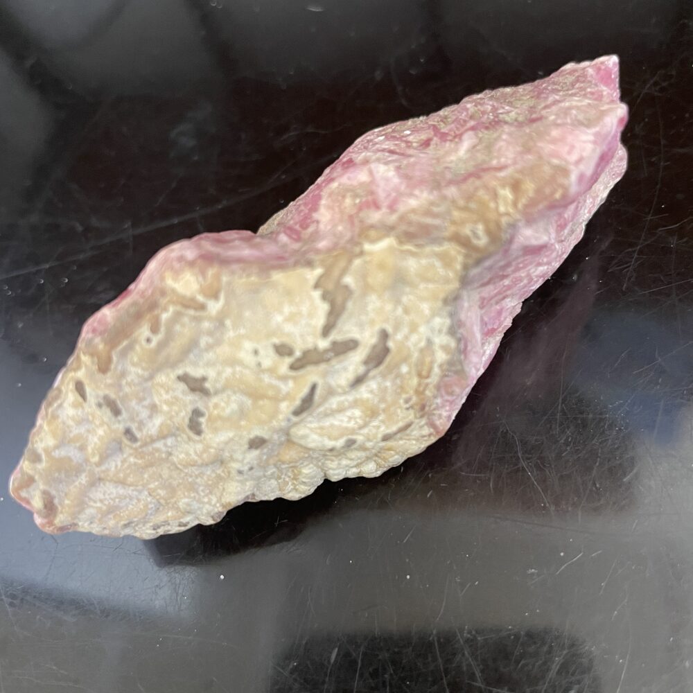 Rhodochrosite specimen with a pink, beige-textured surface and irregular shape, shown on a black background.