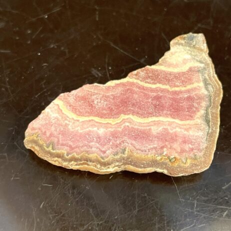 A Rhodochrosite beautiful old stock specimen with pink and white banded layers rests on a dark, reflective surface.