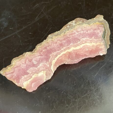 The Rhodochrosite specimen (6.71 grams) has polished pink bands and rough edges, displayed on a dark surface.