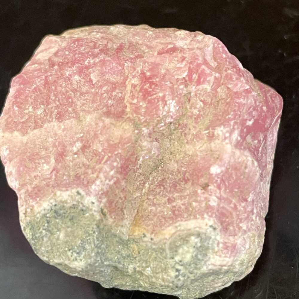 A beautiful Old Stock Rhodochrosite mineral specimen (7.38g) with stunning light and dark patches, displayed on a black surface.